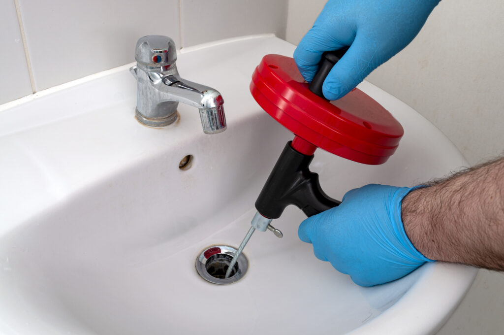 Plumber wearing gloves snaking a bathroom sink drain